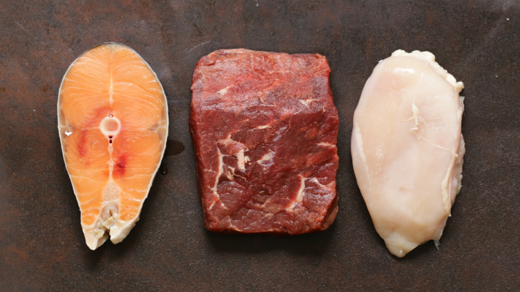 Close-up view of raw salmon, lean beef, and chicken fillet on a rustic surface, showcasing protein-rich foods essential for hair growth as part of African Foods For Longer Hair.