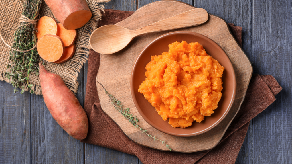 Bowl of mashed sweet potatoes on a wooden board with whole and sliced sweet potatoes, highlighting the nutrients beneficial for hair growth as part of African Foods For Longer Hair.