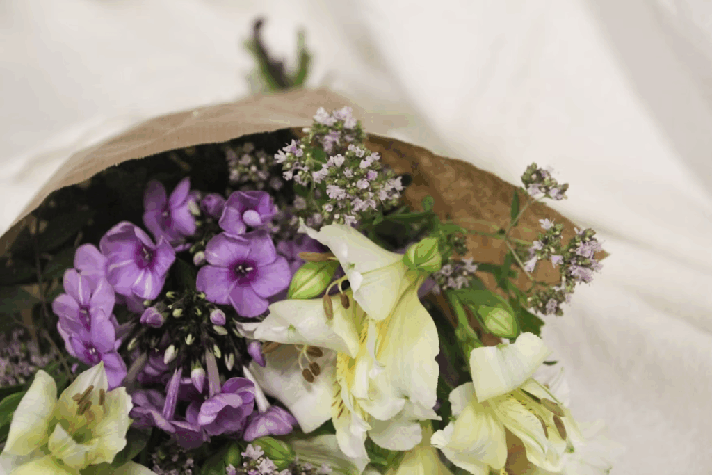 A bouquet of purple and white flowers in a paper bag 